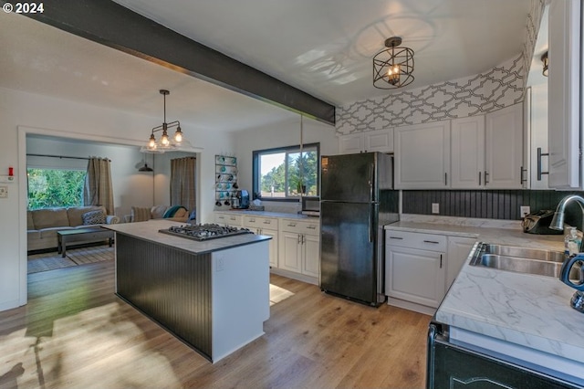 kitchen with black fridge, a kitchen island, decorative light fixtures, white cabinetry, and light hardwood / wood-style floors