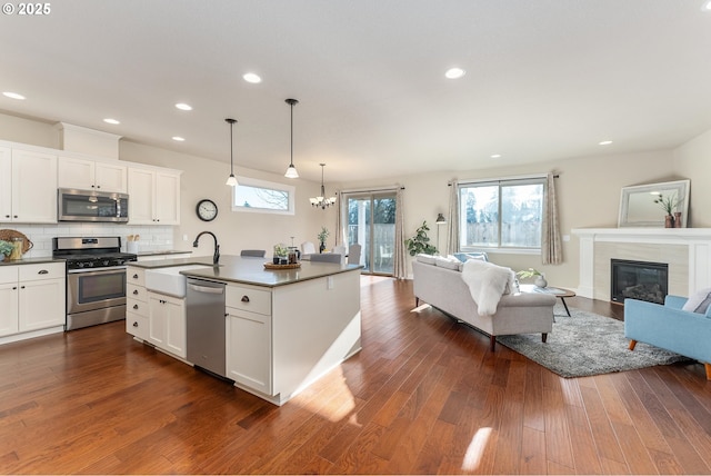 kitchen featuring a tile fireplace, white cabinetry, sink, a kitchen island with sink, and appliances with stainless steel finishes