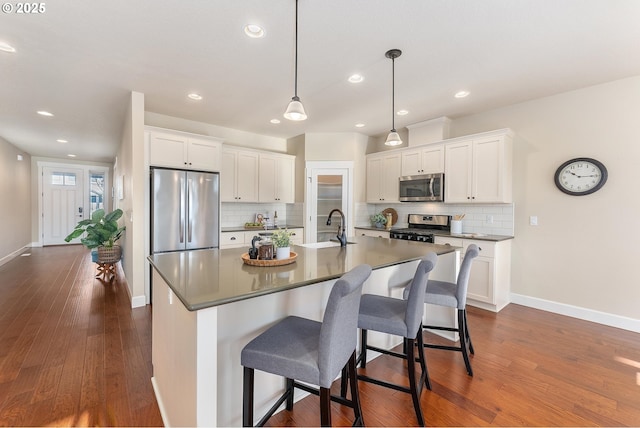 kitchen with stainless steel appliances, a kitchen island with sink, white cabinetry, hanging light fixtures, and a breakfast bar area