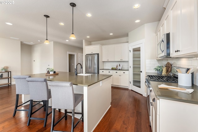 kitchen with stainless steel appliances, dark countertops, a center island with sink, and white cabinetry