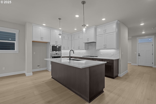 kitchen featuring an island with sink, sink, appliances with stainless steel finishes, white cabinets, and pendant lighting