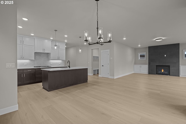 kitchen with a center island with sink, pendant lighting, a large fireplace, white cabinets, and gas cooktop