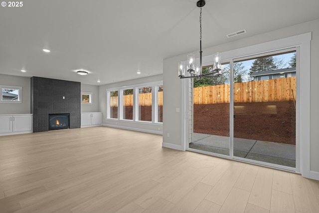 unfurnished living room featuring a large fireplace, an inviting chandelier, and light hardwood / wood-style floors