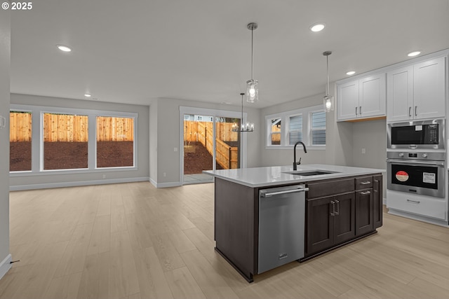 kitchen featuring stainless steel appliances, white cabinets, decorative light fixtures, sink, and a kitchen island with sink