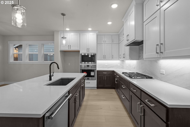 kitchen featuring appliances with stainless steel finishes, decorative light fixtures, an island with sink, and white cabinets