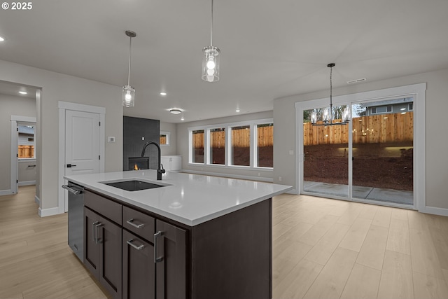 kitchen featuring a center island with sink, dark brown cabinetry, stainless steel dishwasher, light hardwood / wood-style floors, and sink