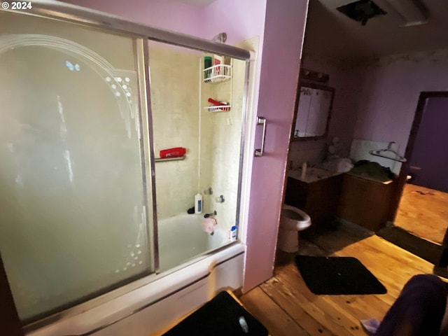 bathroom with toilet, hardwood / wood-style floors, and combined bath / shower with glass door