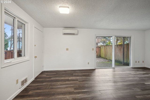 empty room featuring a wall mounted AC, plenty of natural light, and dark hardwood / wood-style floors