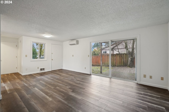 unfurnished room with a healthy amount of sunlight, a wall unit AC, and dark wood-type flooring