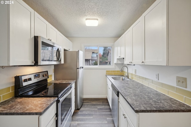 kitchen featuring appliances with stainless steel finishes, a textured ceiling, dark wood-type flooring, sink, and white cabinets