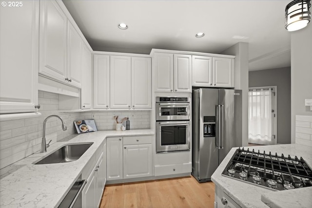 kitchen featuring light stone countertops, white cabinetry, appliances with stainless steel finishes, and a sink