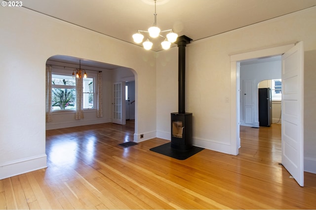 spare room with a notable chandelier, light hardwood / wood-style flooring, and a wood stove