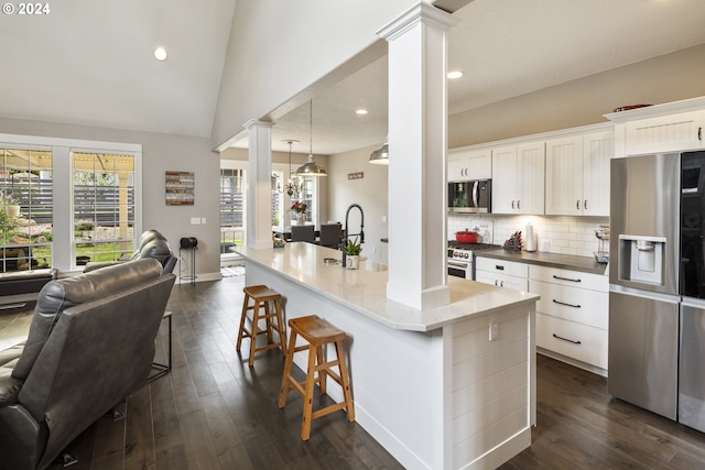 kitchen with ornate columns, dark hardwood / wood-style flooring, a kitchen island with sink, tasteful backsplash, and stainless steel appliances