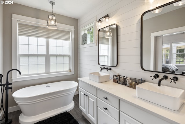 bathroom featuring wood walls, a tub to relax in, hardwood / wood-style floors, and dual bowl vanity