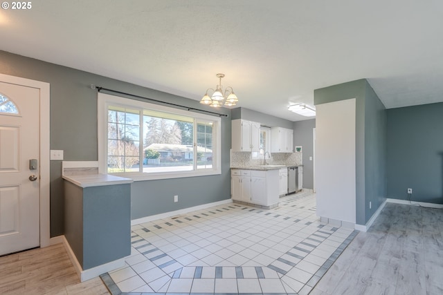 kitchen with decorative light fixtures, white cabinets, dishwasher, a notable chandelier, and backsplash