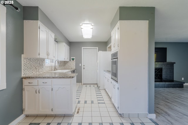 kitchen featuring light stone countertops, stainless steel oven, white cabinets, and backsplash