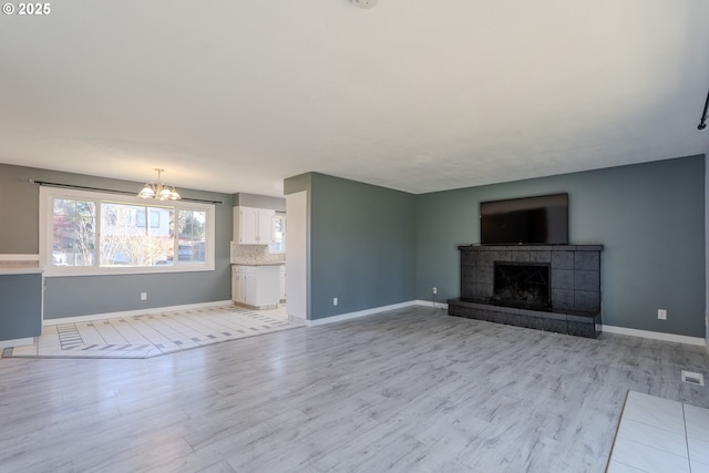 unfurnished living room featuring a tiled fireplace, a notable chandelier, and light wood-type flooring