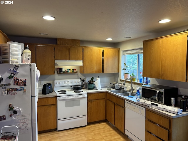 kitchen with a textured ceiling, white appliances, sink, and light hardwood / wood-style flooring