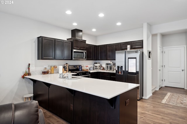 kitchen featuring light wood-type flooring, stainless steel appliances, sink, kitchen peninsula, and a breakfast bar