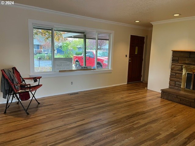 sitting room with a stone fireplace, hardwood / wood-style floors, crown molding, and a textured ceiling