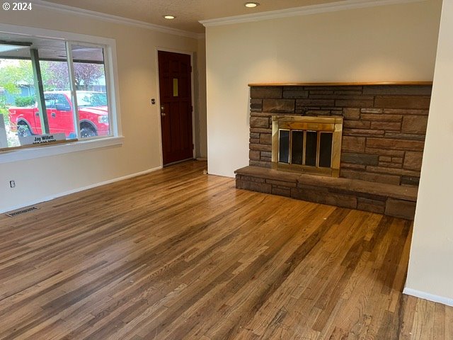 unfurnished living room featuring a stone fireplace, wood-type flooring, and ornamental molding