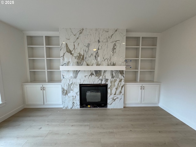 unfurnished living room with light wood finished floors, built in shelves, baseboards, and a stone fireplace