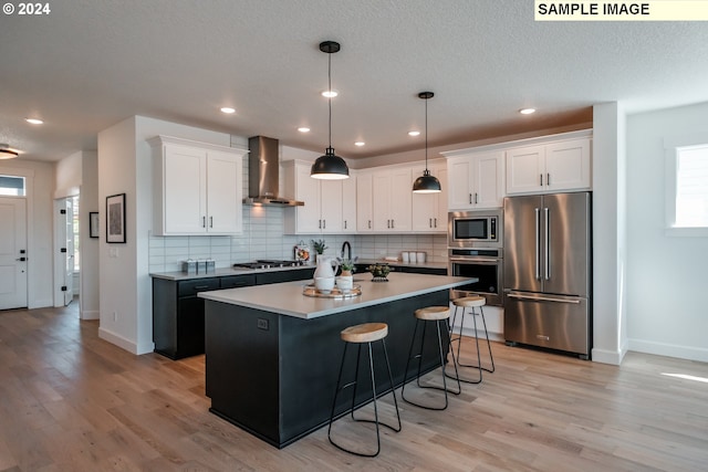 kitchen with wall chimney exhaust hood, stainless steel appliances, hanging light fixtures, and white cabinets