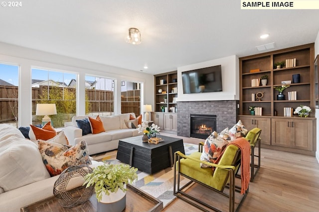 living room with a brick fireplace, built in features, and light hardwood / wood-style floors