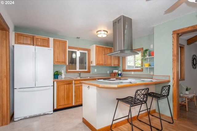 kitchen featuring a kitchen bar, kitchen peninsula, island exhaust hood, white appliances, and pendant lighting