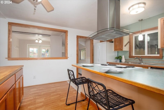 kitchen with island range hood, white appliances, pendant lighting, light hardwood / wood-style flooring, and sink