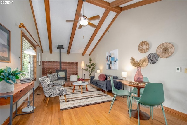 living room with ceiling fan, a wood stove, wood-type flooring, high vaulted ceiling, and beam ceiling