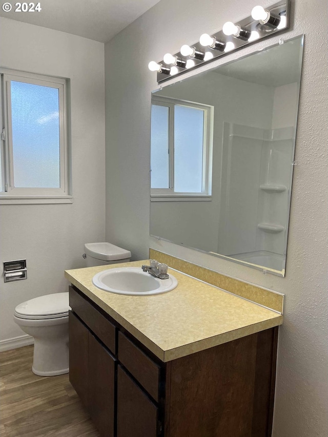 bathroom with walk in shower, hardwood / wood-style floors, vanity, and toilet