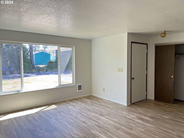 unfurnished room with a textured ceiling and light hardwood / wood-style floors