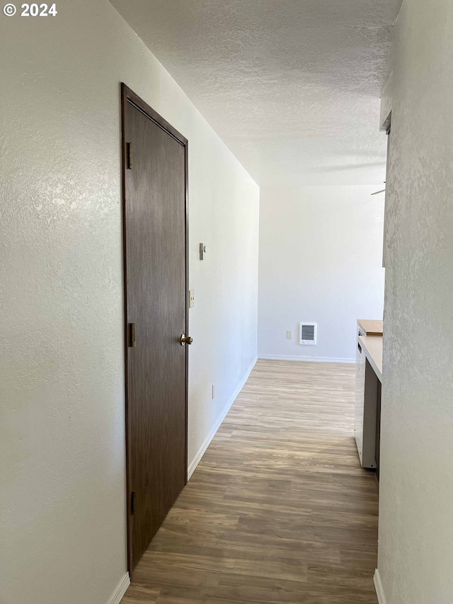hallway with light wood-type flooring and a textured ceiling
