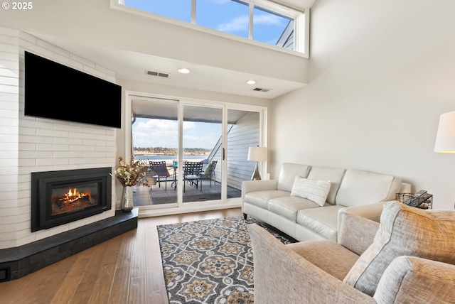 living room with a large fireplace, visible vents, wood finished floors, and recessed lighting