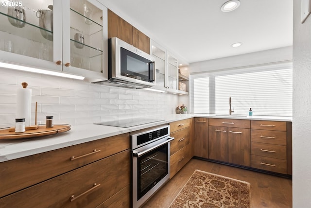 kitchen with dark wood-style flooring, backsplash, appliances with stainless steel finishes, glass insert cabinets, and a sink