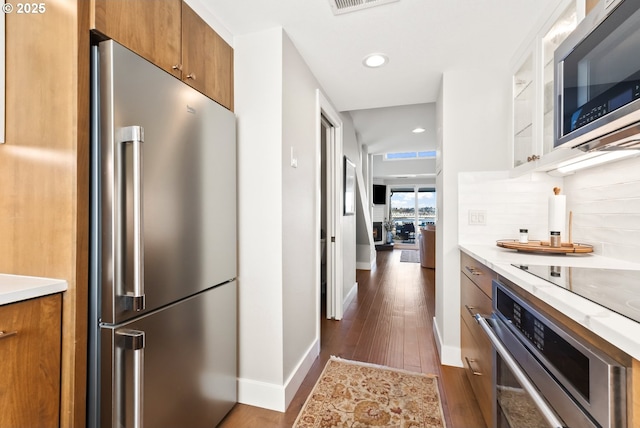 kitchen with dark wood-style floors, stainless steel appliances, tasteful backsplash, and brown cabinetry