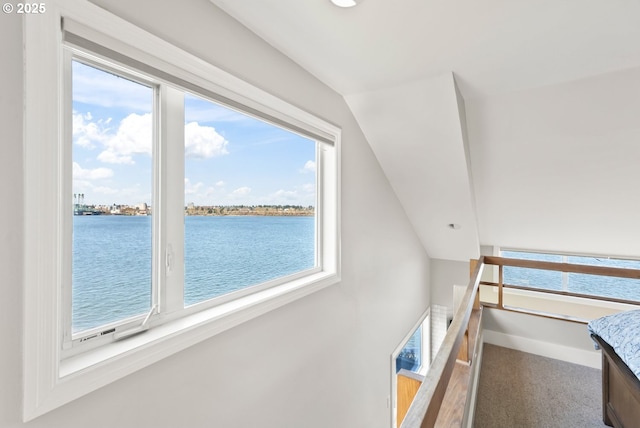 interior space with a water view, carpet flooring, vaulted ceiling, an upstairs landing, and baseboards