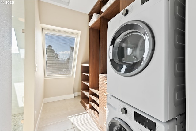 washroom with stacked washer and dryer, laundry area, baseboards, and light tile patterned floors