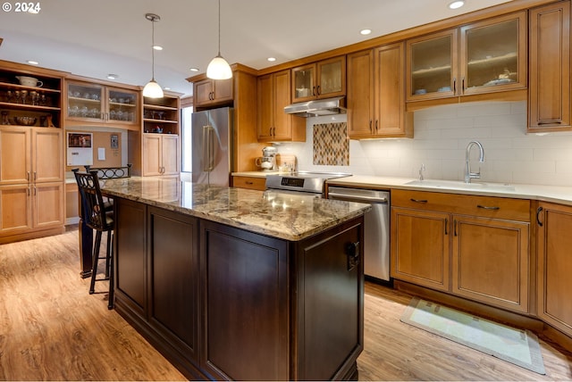 kitchen with stainless steel appliances, light wood-type flooring, backsplash, a center island, and sink