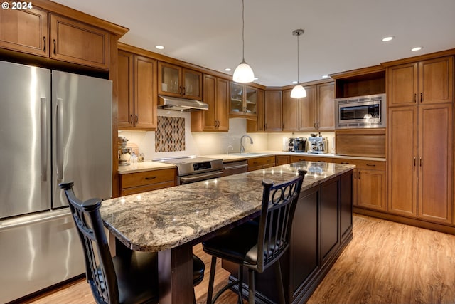 kitchen featuring hanging light fixtures, light wood-type flooring, appliances with stainless steel finishes, a breakfast bar area, and tasteful backsplash