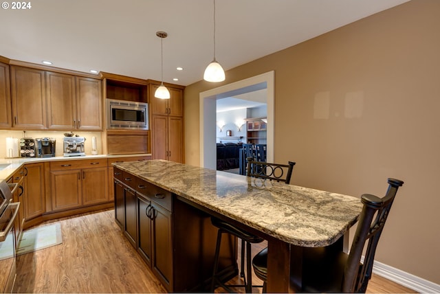 kitchen with a kitchen breakfast bar, light hardwood / wood-style flooring, pendant lighting, stainless steel microwave, and light stone counters