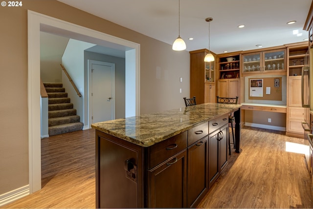 kitchen featuring dark brown cabinets, light wood-type flooring, pendant lighting, light stone counters, and a kitchen island