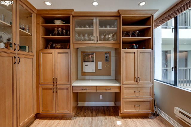 interior space with built in desk, baseboard heating, and light wood-type flooring