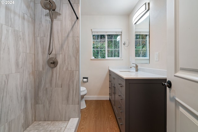 bathroom with a tile shower, vanity, wood-type flooring, and toilet