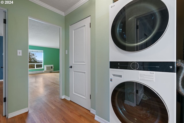 laundry room with crown molding, stacked washer and dryer, wood-type flooring, and a textured ceiling