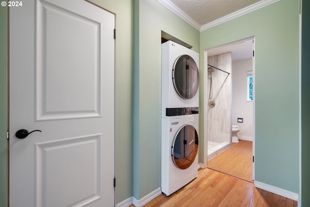 clothes washing area featuring a textured ceiling, hardwood / wood-style flooring, crown molding, and stacked washer / drying machine