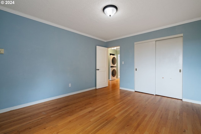 unfurnished bedroom featuring stacked washing maching and dryer, a textured ceiling, crown molding, wood-type flooring, and a closet