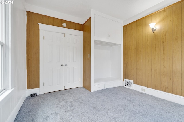 unfurnished bedroom featuring a closet, wood walls, and carpet floors