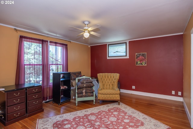 living area with baseboards, hardwood / wood-style floors, a ceiling fan, and crown molding